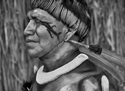 Tsaná, cantor de música tradicional do Alto Xingu, um presente que ele herdou de seu pai, o maestro Tagukagé. Nessa foto de Sebastião Salgado, Tsaná está usando um colar de conchas de caracóis e tem o corpo pintado de urucum.