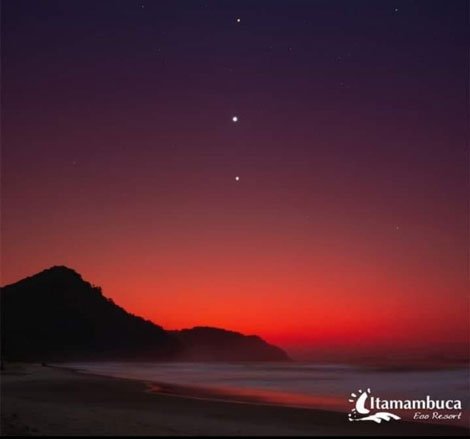 Amanhecer na praia de Itamambuca, com pontos luminosos no céu.