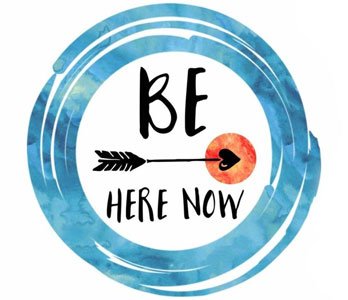 Círculo azul com a inscrição Be Here Now e um coração.